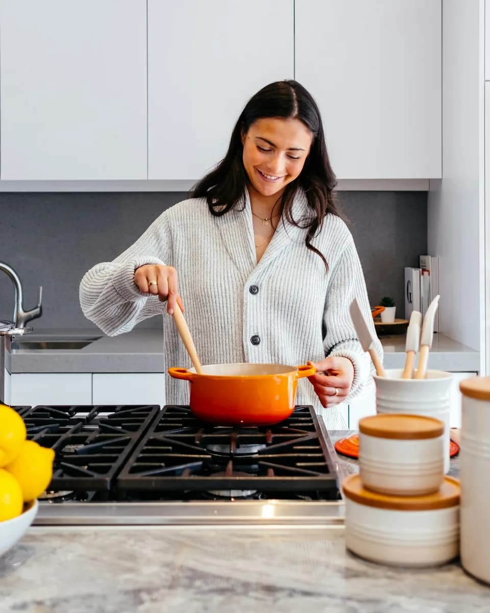 A woman stirring a pot on the stove in a bright kitchen