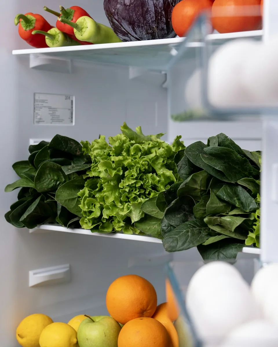 An open fridge with fresh greens, oranges and eggs