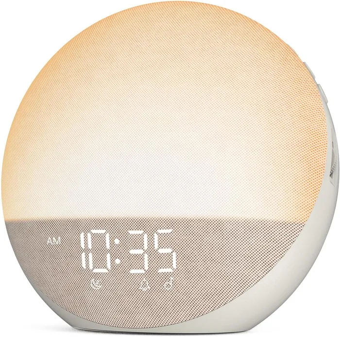 A round bedside sunrise alarm clock glowing warm amber above a digital time display.