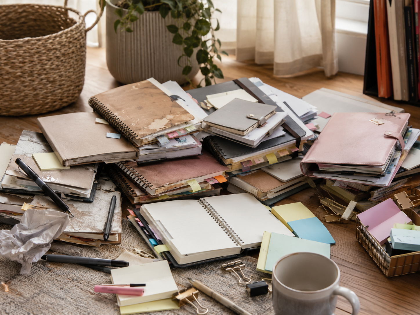 A messy collection of old planners, notebooks, sticky notes, pens and papers, representing abandoned ADHD systems and repeated attempts to get organized.